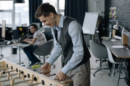 Young man enjoying a game of foosball in a modern office space, depicting a relaxed work environment.