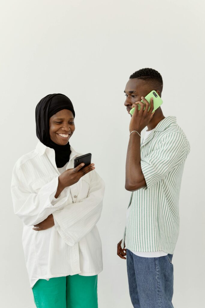 A joyful Muslim couple engages in conversation while using mobile phones indoors.