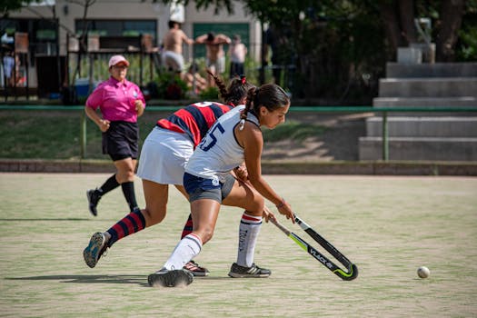 Two young girls in action during a thrilling field hockey game outdoors.