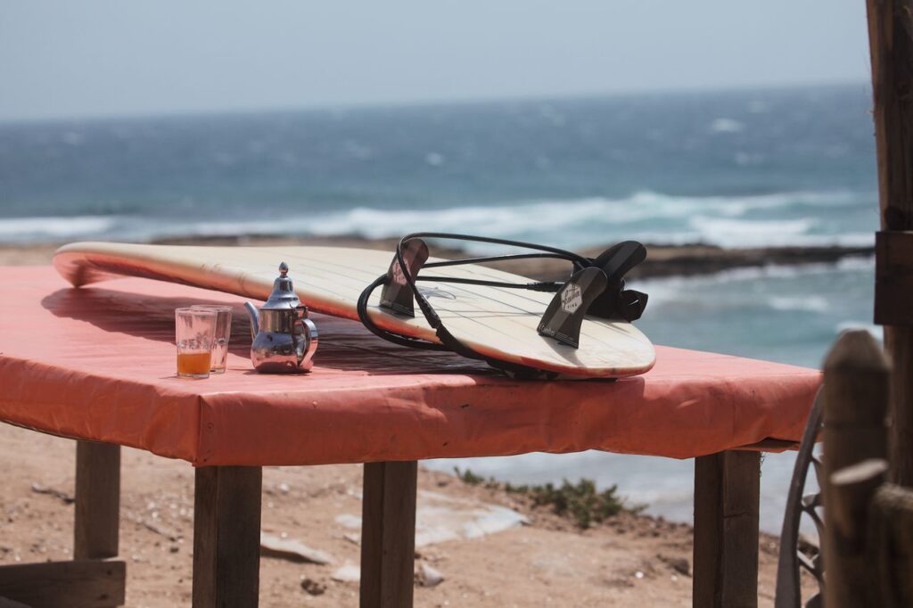 Surfboard and mint tea on a table by the ocean in Morocco, capturing a laid-back ambiance.