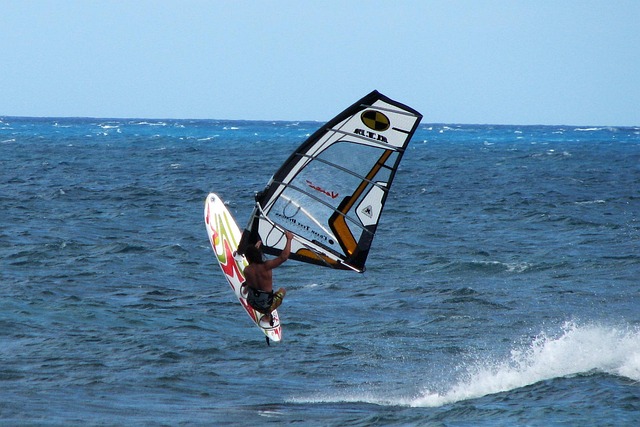Un windsurfeur soulève sa planche au-dessus de la mer, sur une eau calme et parfaitement plate, sans aucune vague.